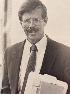 Dr. Mathews stands in a suit holding books.